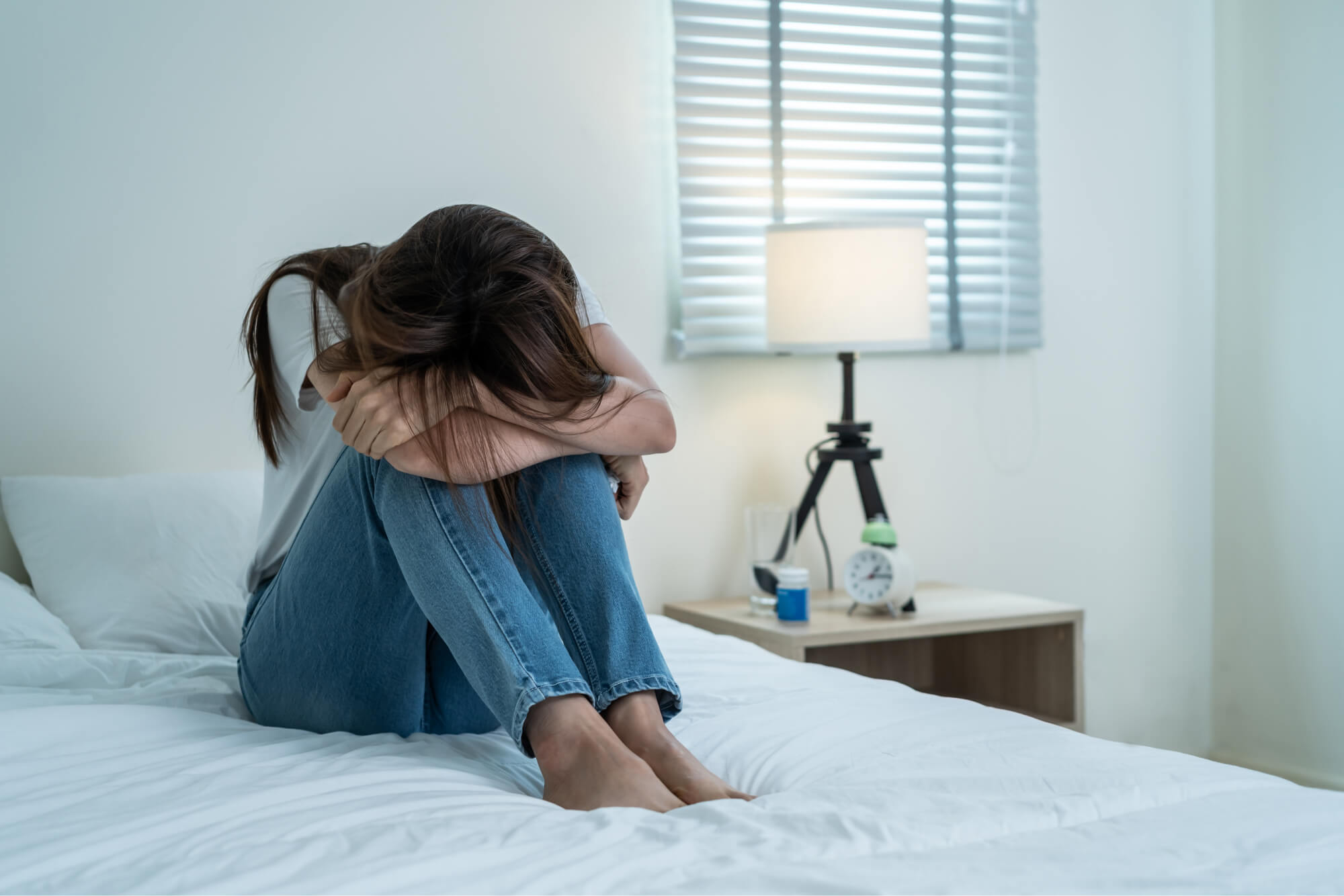 A woman sitting on her bed and hiding her face.